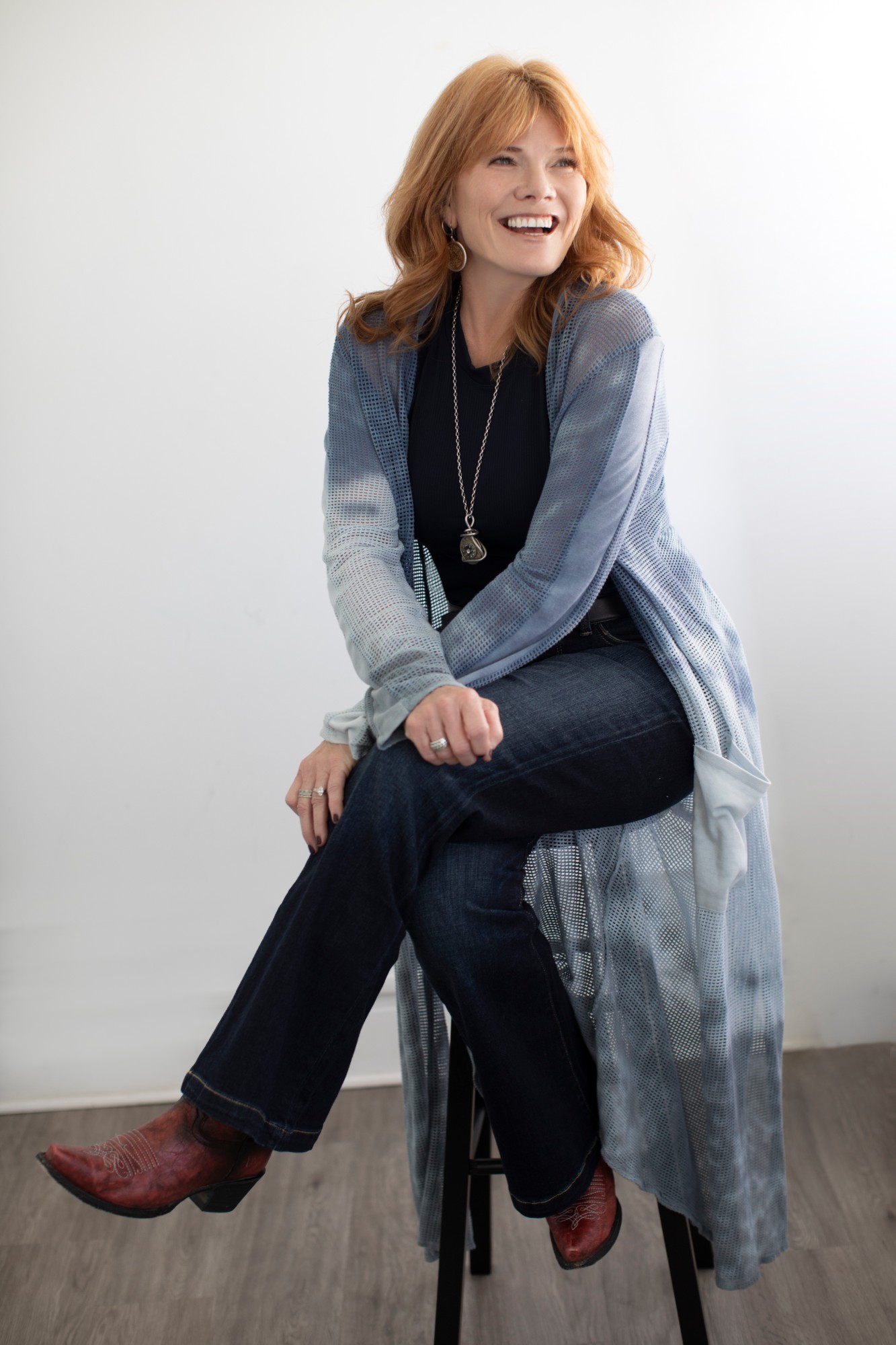 Michelle Melton Cox, book coach, laughing on a stool in jeans and red cowboy boots